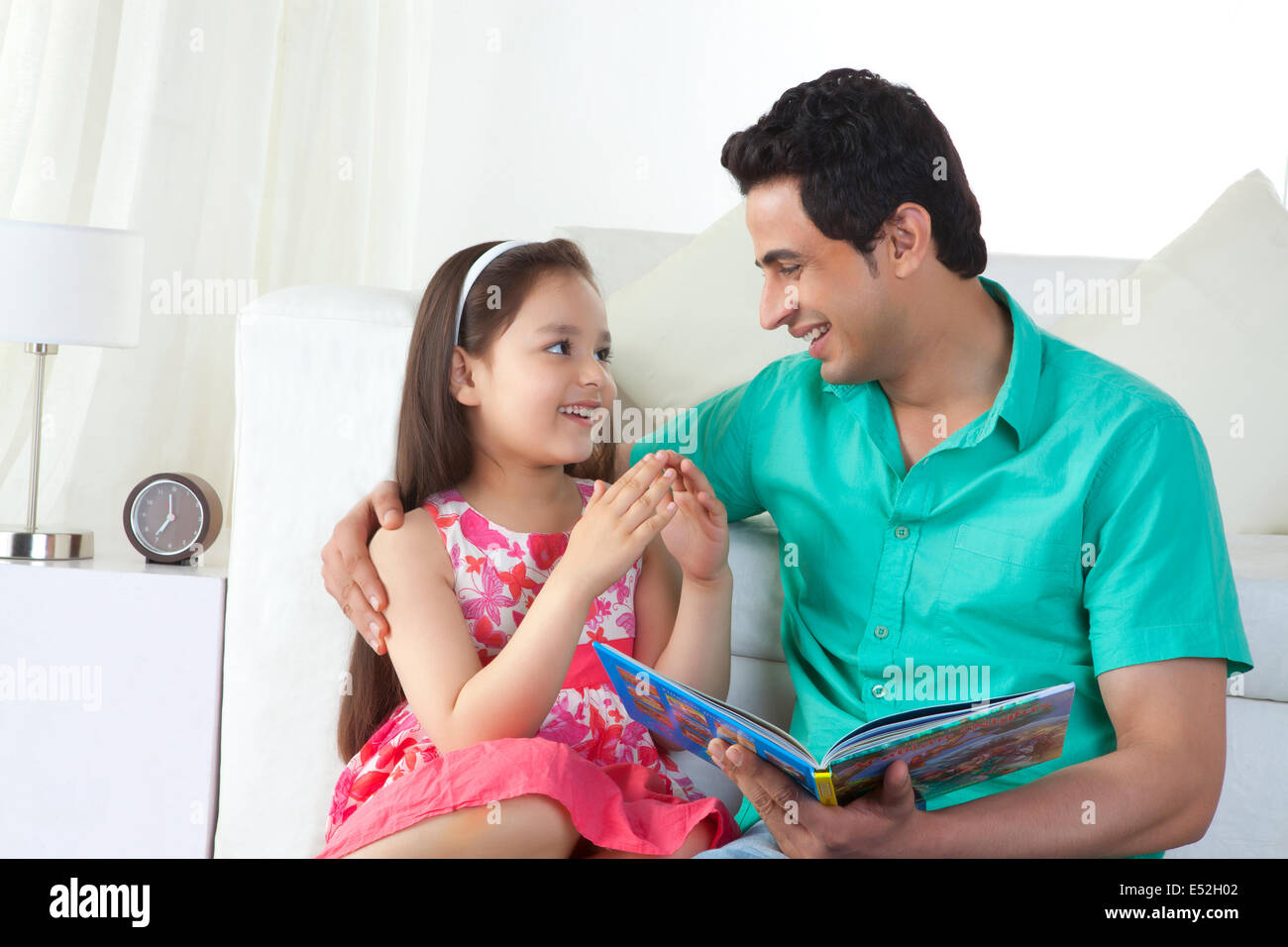 Girl explaining story to father on sofa at home Stock Photo