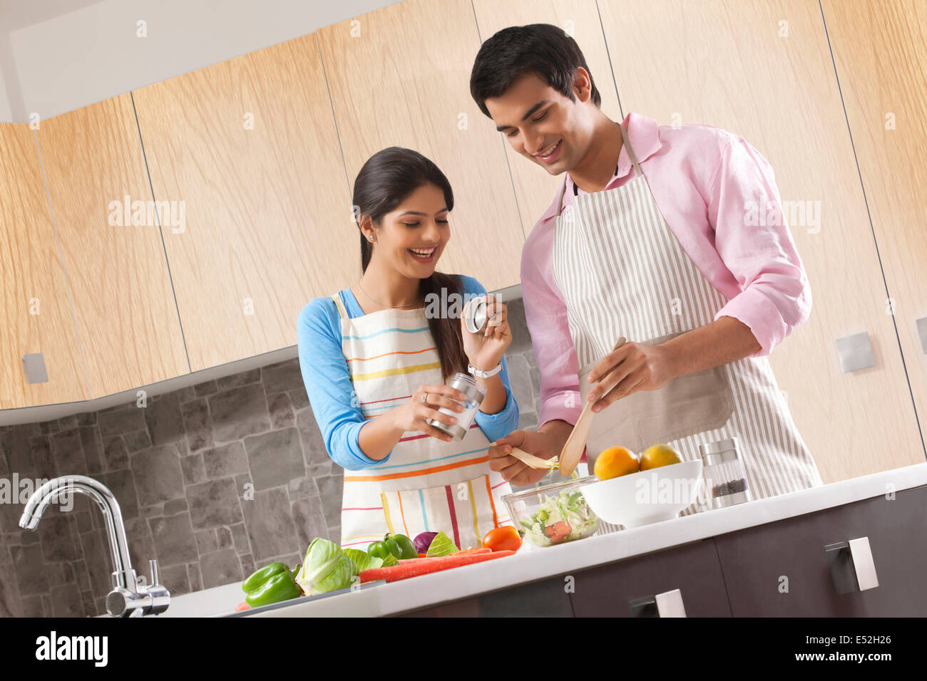 Smiling young couple preparing fresh salad in kitchen Stock Photo