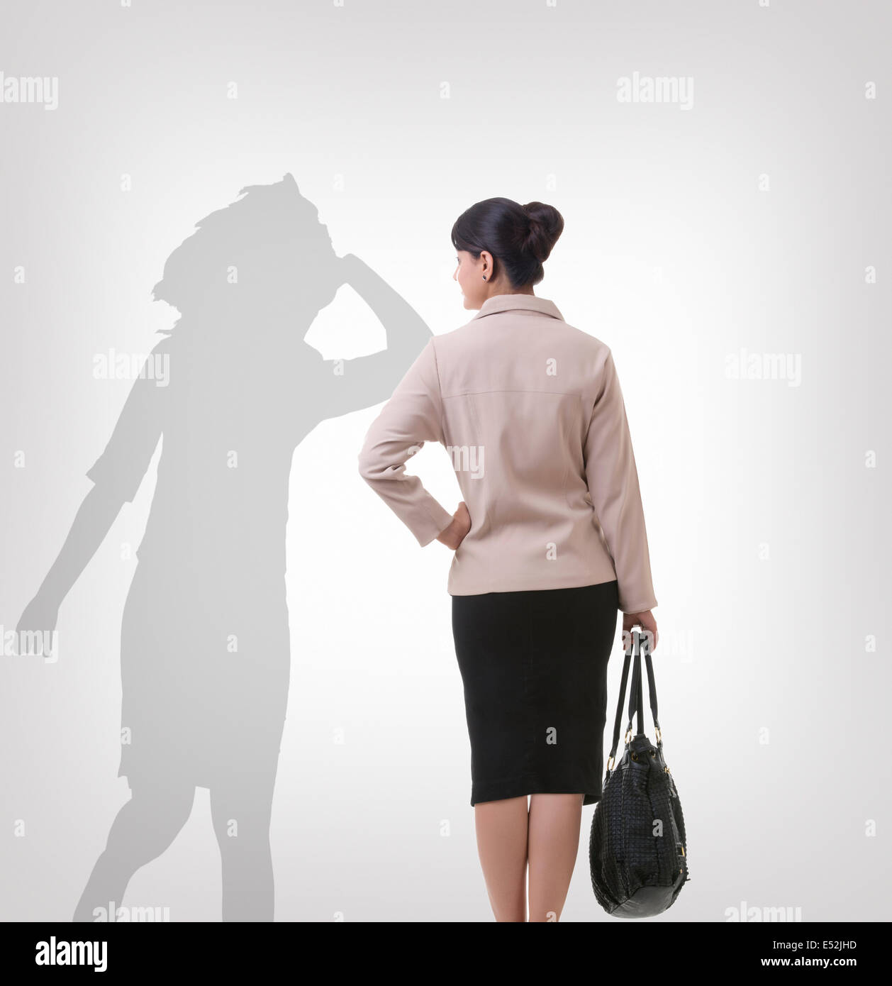 Rear view of businesswoman looking at her shadow dancing over gray background Stock Photo