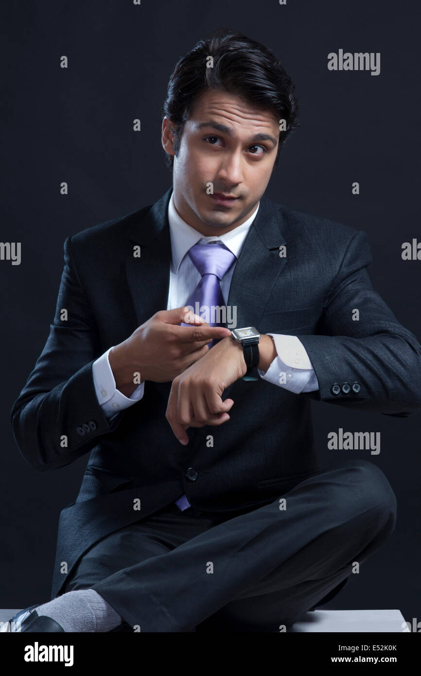 Young businessman checking time against black background Stock Photo ...