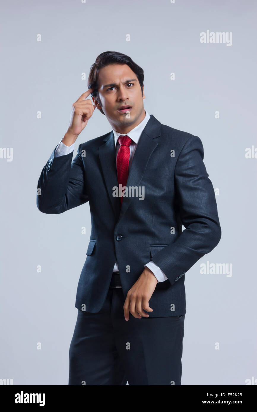 Confused businessman scratching head against gray background Stock Photo