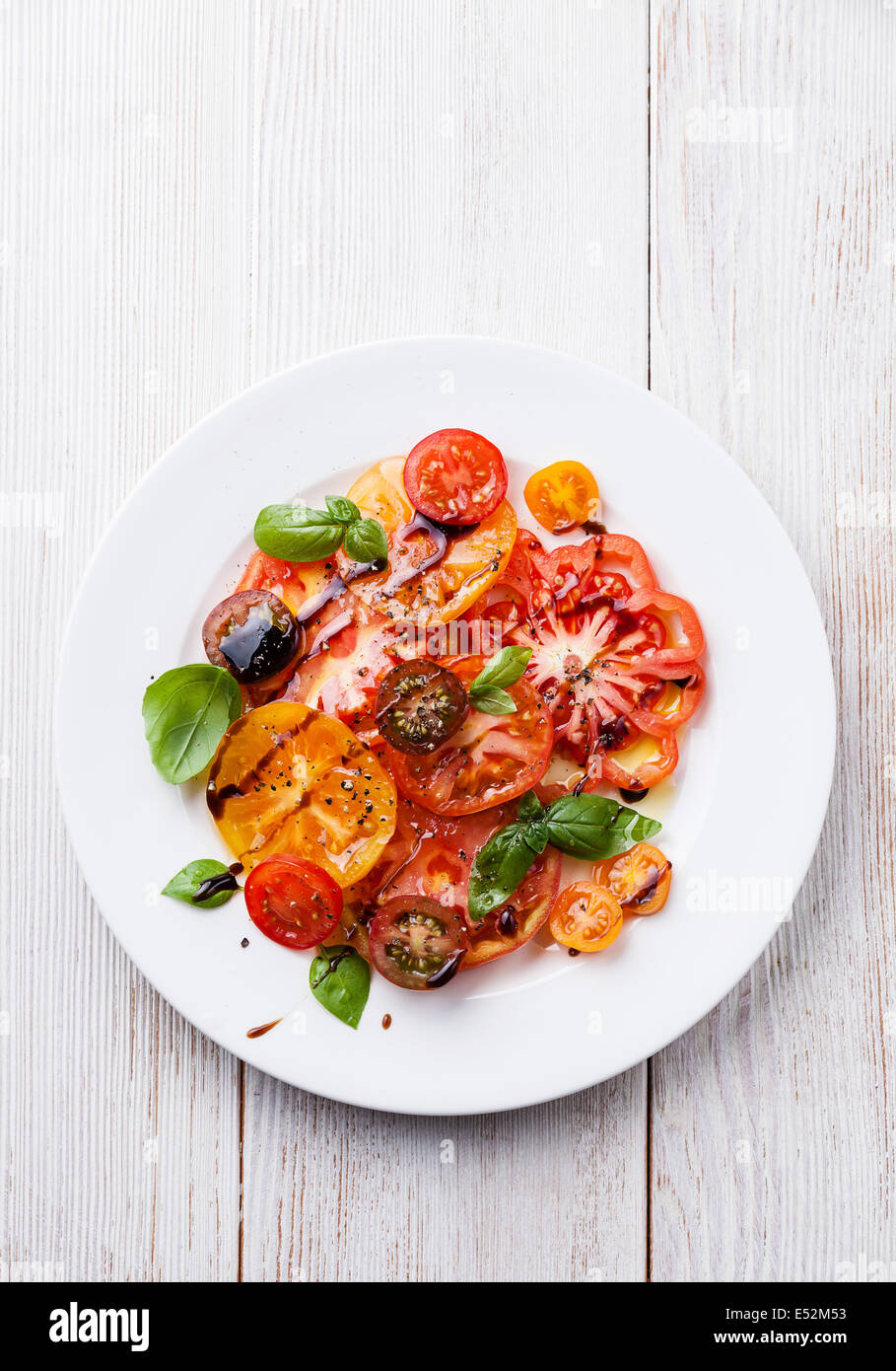 Ripe fresh colorful tomatoes salad with olive oil and balsamic vinegar on white wooden background Stock Photo