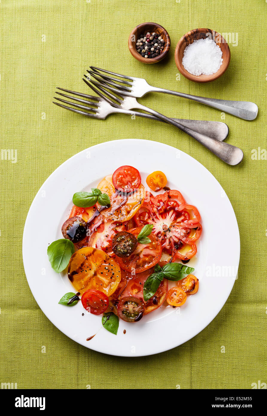 Ripe fresh colorful tomatoes salad with olive oil and balsamic vinegar on green background Stock Photo