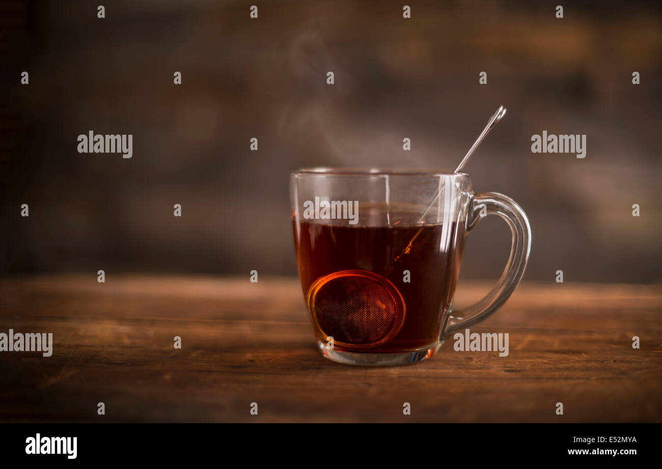 Clear glass of steaming hot tea with infuser on wooden, rustic suface. Stock Photo