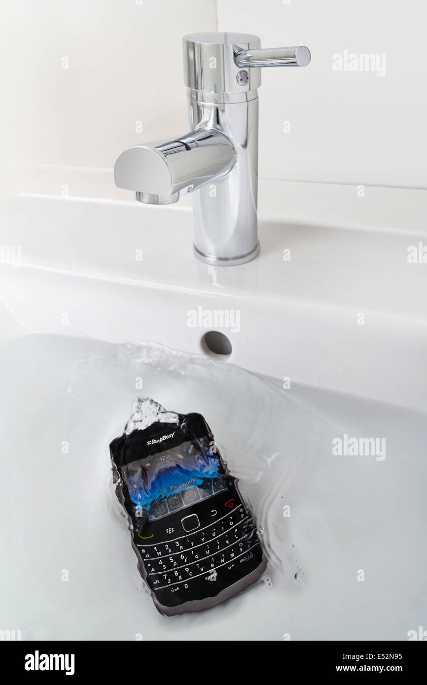 blackberry mobile cell phone dropped in bathroom sink full of water Stock Photo