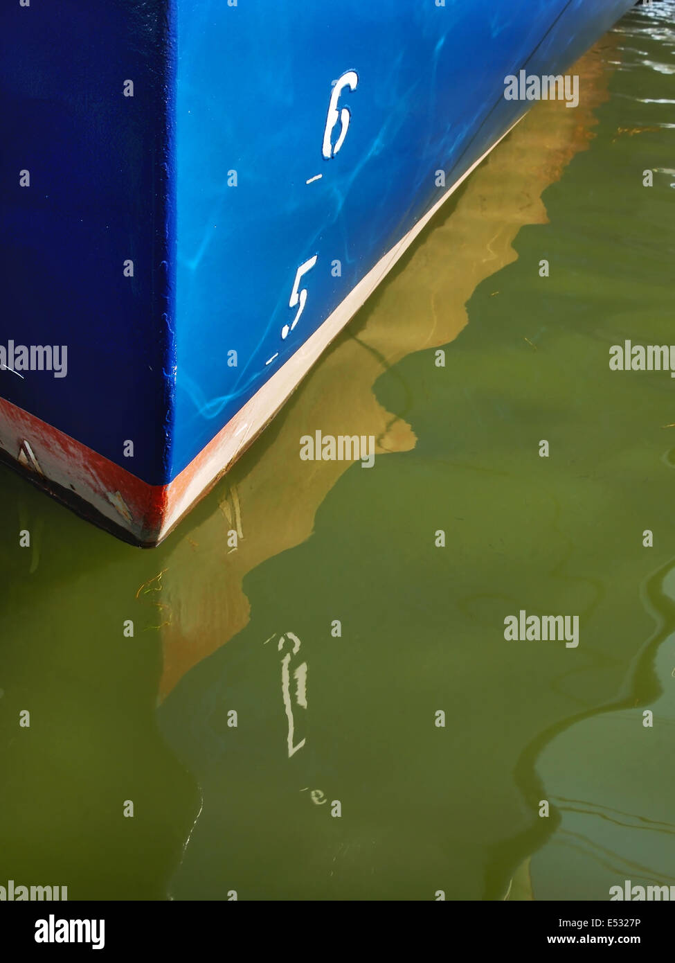 A bright blue boat hull with the numbers 6 and 5, and it's reflection on the surrounding water. Stock Photo