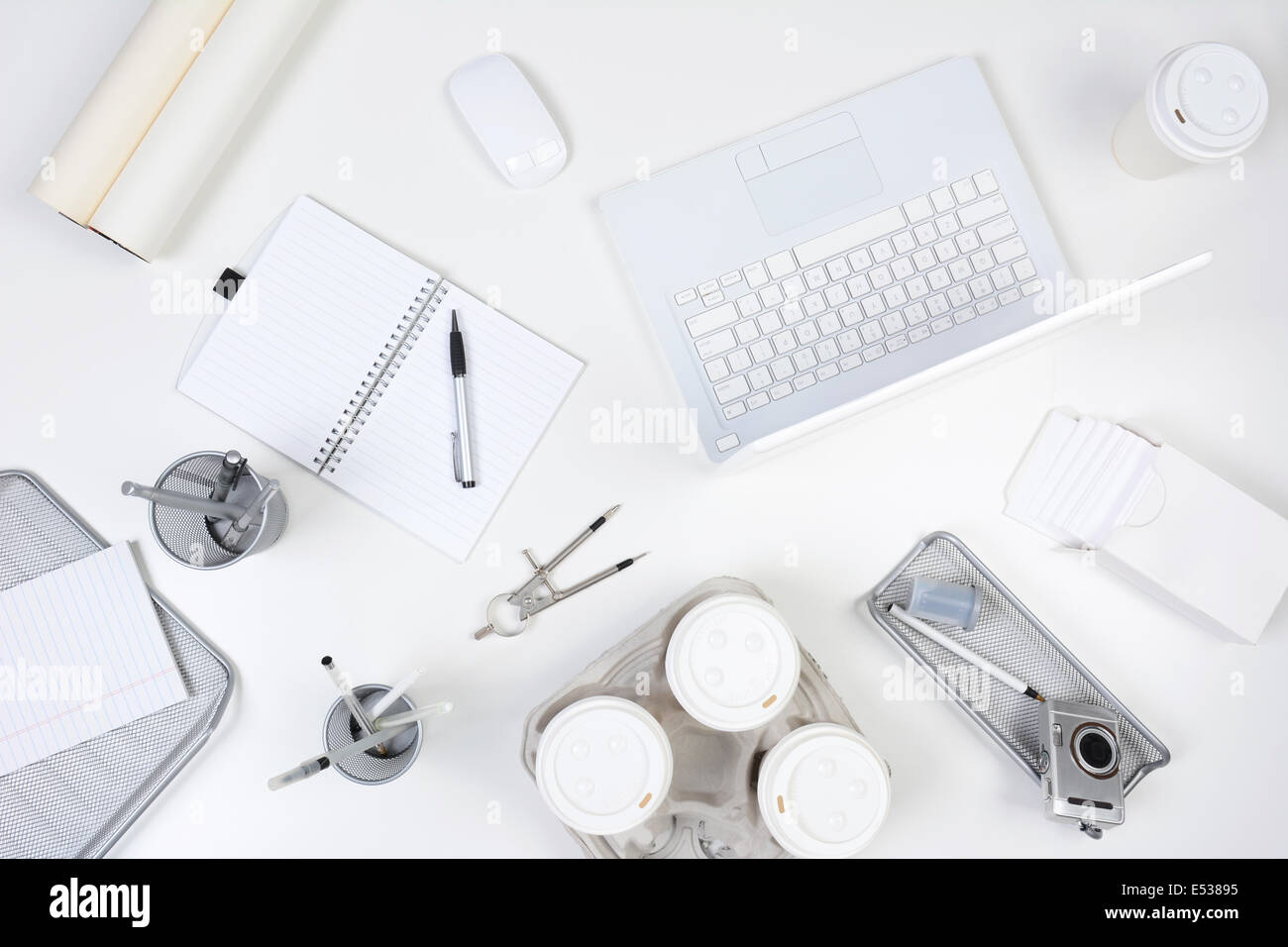 High angle shot of a white desk with primarily white and silver office objects. Items include, laptop computer, pad, pens Stock Photo