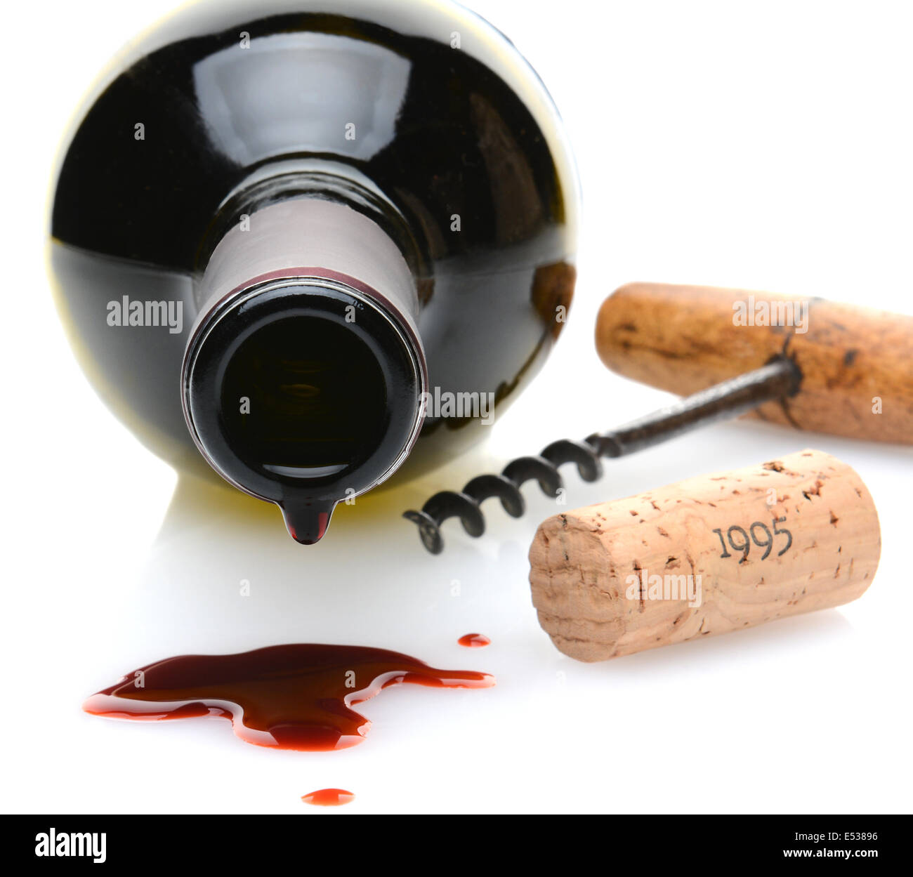 Closeup of a red wine bottle with a drip and wine spill in the foreground. A cork screw and cork to one side Stock Photo