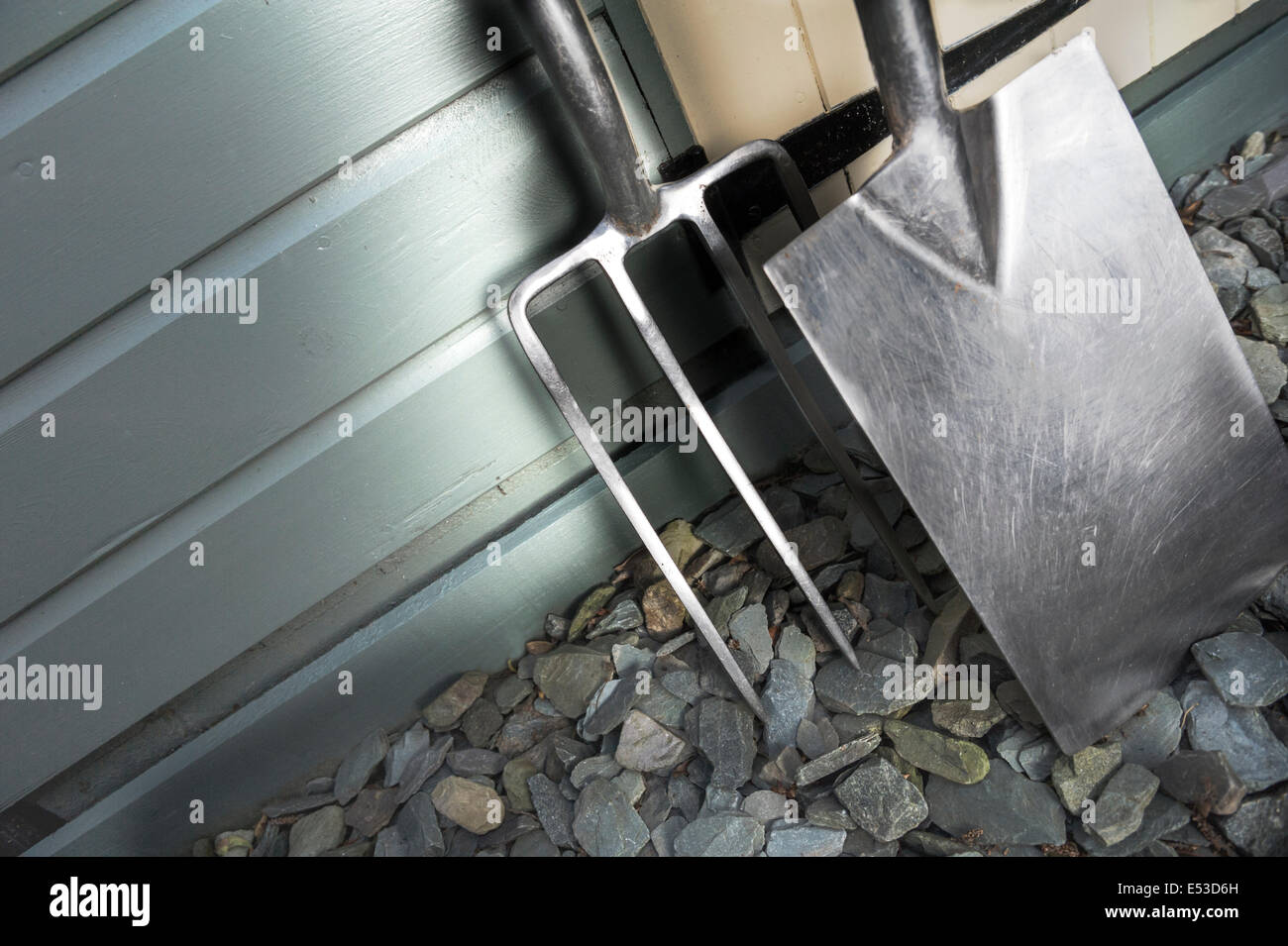 Garden fork and spade leaning against a painted shed Stock Photo