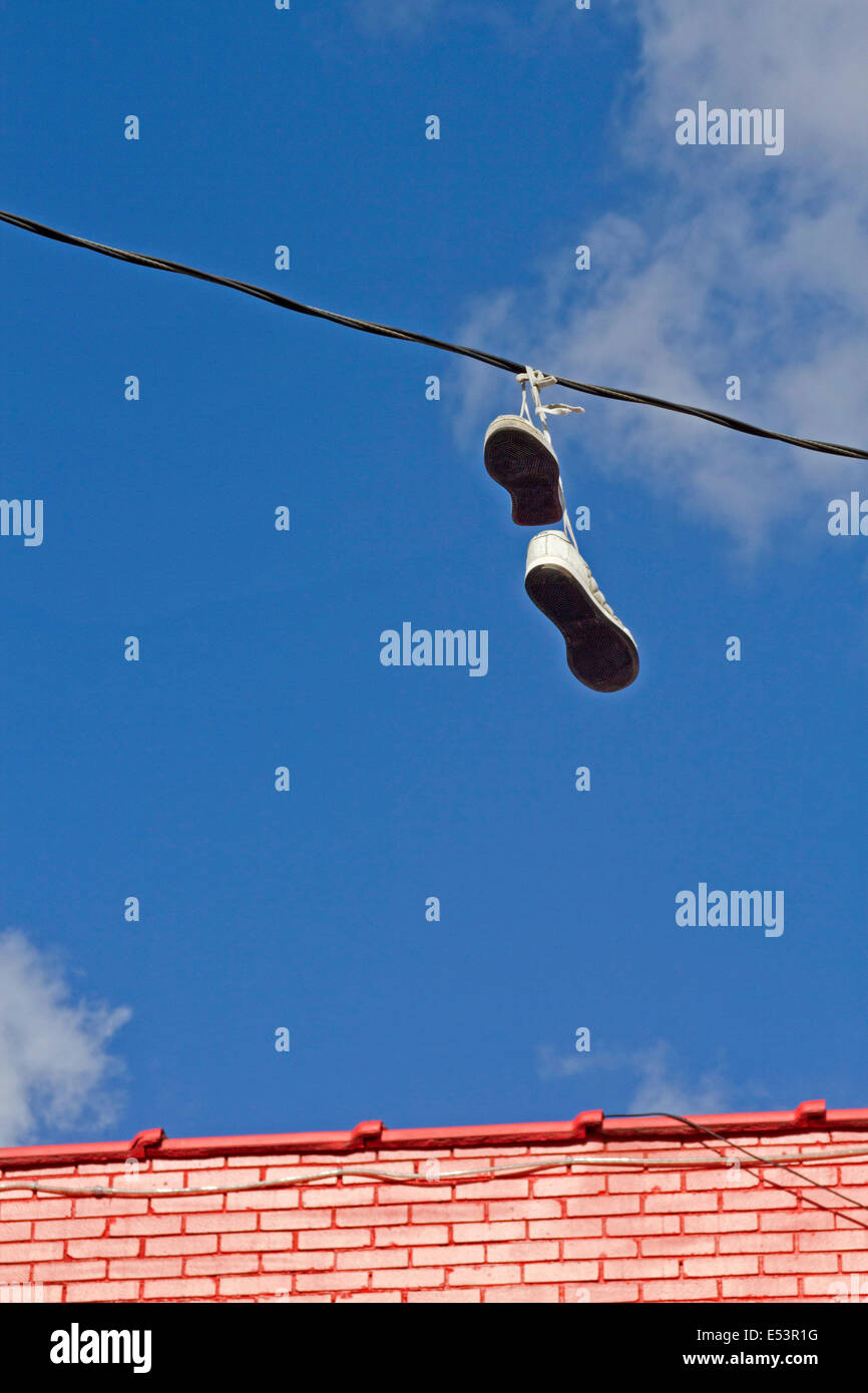 Unreachable shoes hanging over a wire by its tied shoelaces, thrown up there as a prank Stock Photo