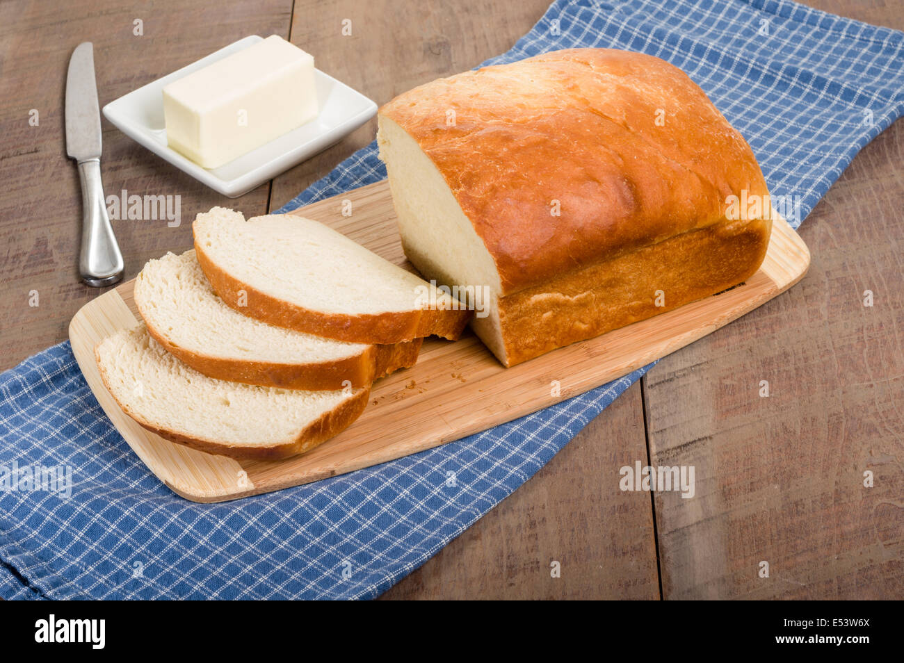 A loaf of bread sliced on a cutting board with a butter plate Stock ...
