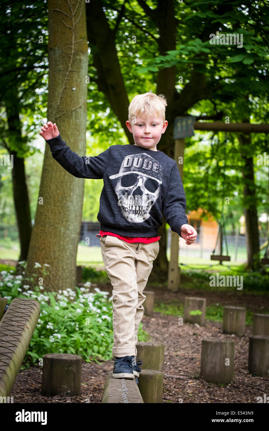 Boy walks confidently along balancing beam on adventure playground Stock Photo