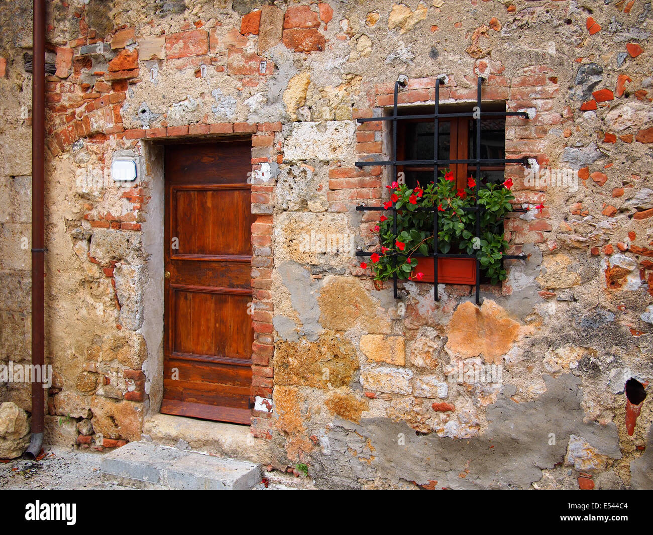 Old wooden door in a brick facade with flowers of a house in an old Italian town. Stock Photo