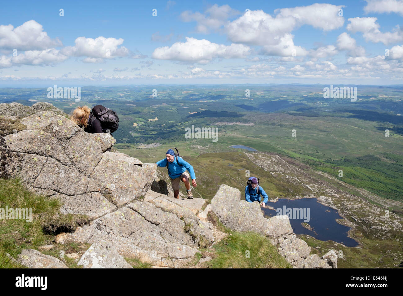 Three hikers scrambling up rocks on Carnedd Moel Siabod Daear Ddu east ridge with view down to Llyn y Foel Snowdonia National Park (Eryri) Wales UK Stock Photo