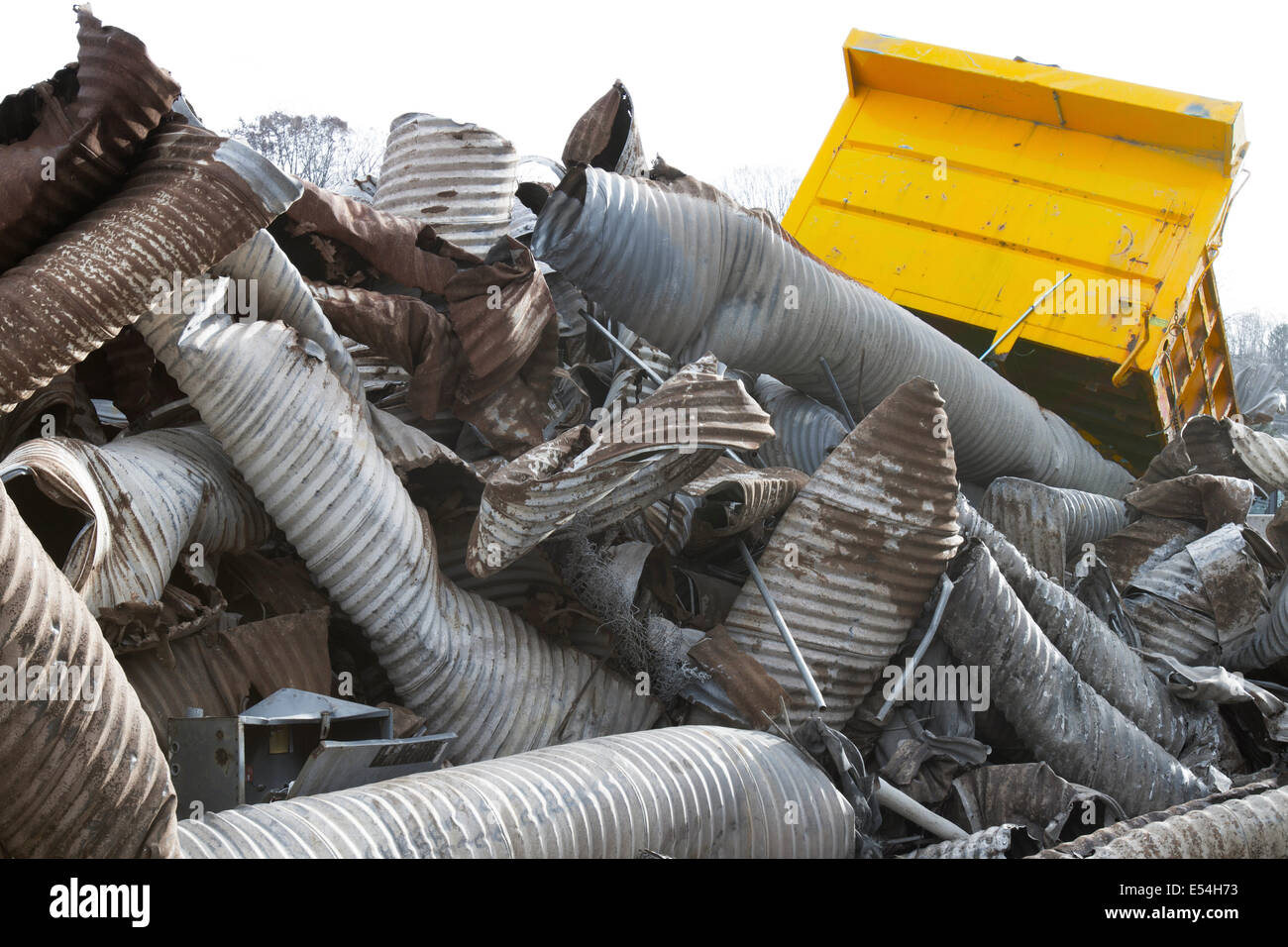 Scrap heap of rusting discarded drainage pipes with yellow tractor wagon Stock Photo