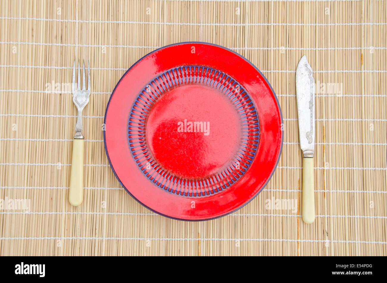 empty red ceramic dinner plate with knife and fork on table Stock Photo