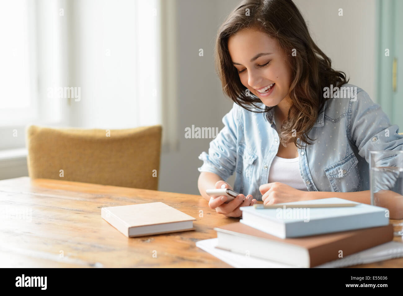 Teenage girl at home looking mobile phone smiling studying books Stock Photo