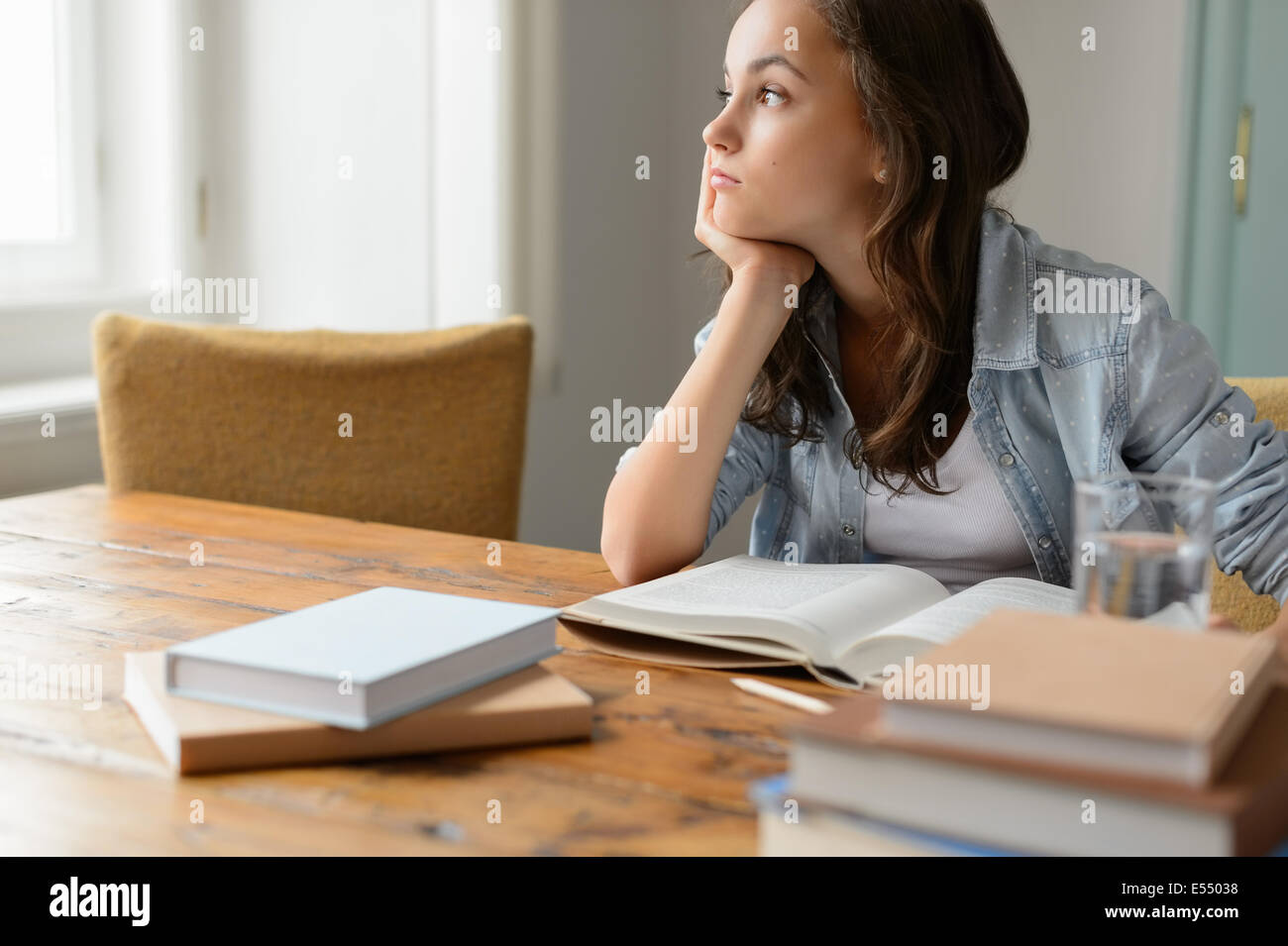 Bored student girl sitting home living room looking away read book Stock Photo