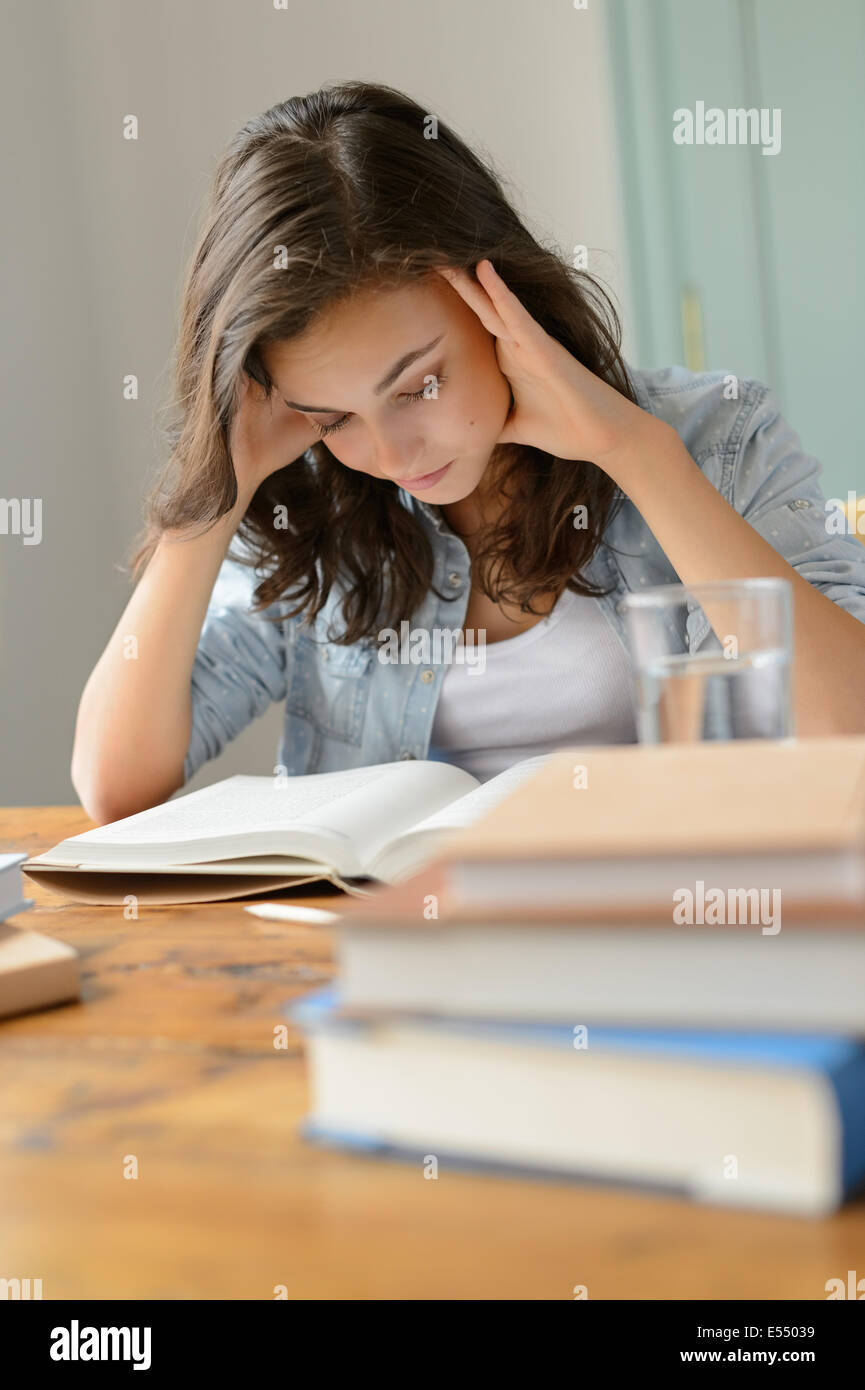 Student teenage girl concentrate reading book home holding her head Stock Photo