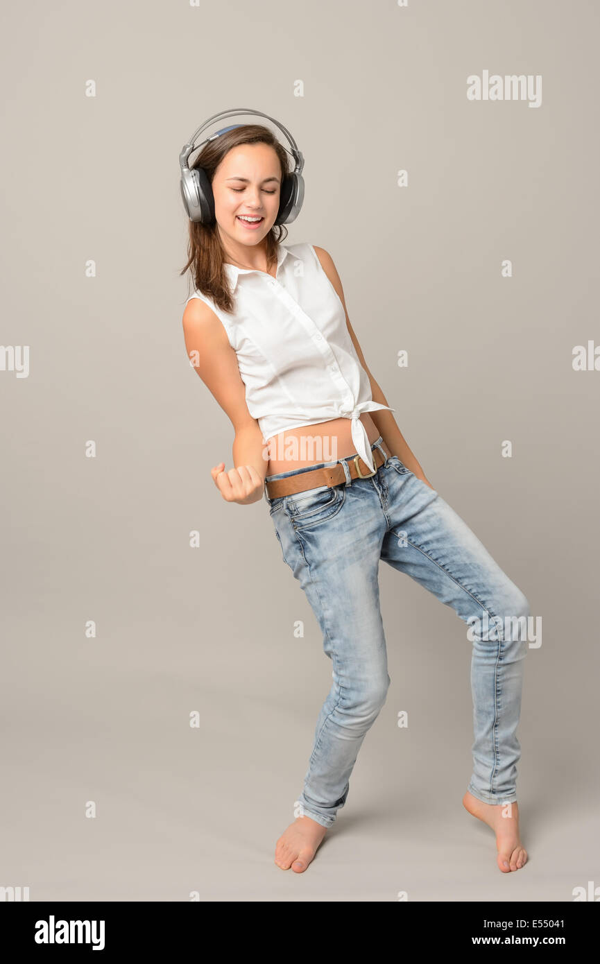 Dancing girl with headphones singing enjoy music full length on gray Stock Photo