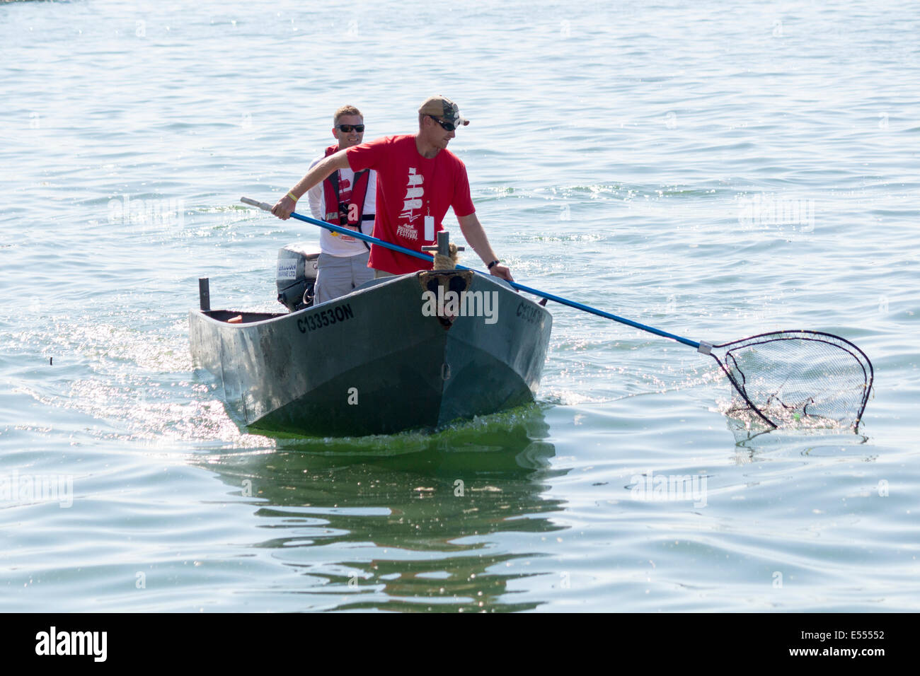Two young men in small watercraft using net to clear debris out of the water. Stock Photo