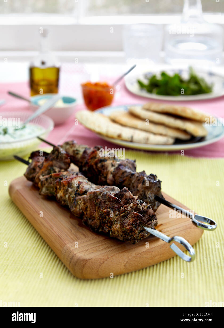barbecued Greek Souvlaki Chicken Kebabs with Tzatziki Sauce on board in front of window with pita bread Stock Photo