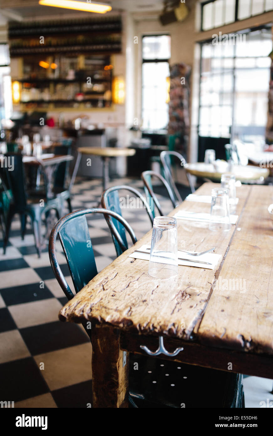 Community table with metal chairs and checkered floor in modern industrial restaurant. Stock Photo