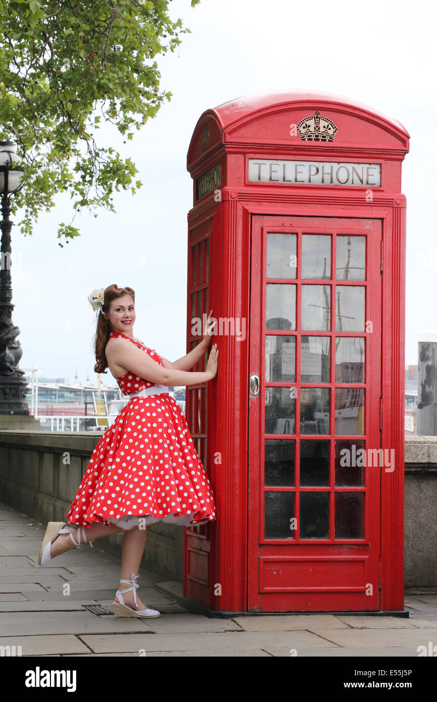 Girl in red polka dot dress standing next to phone box Stock Photo