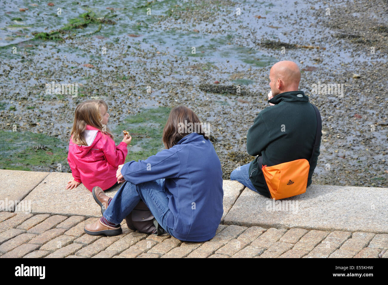 family sitting on harbour wall, Brixham, Devon, England, UK Stock Photo