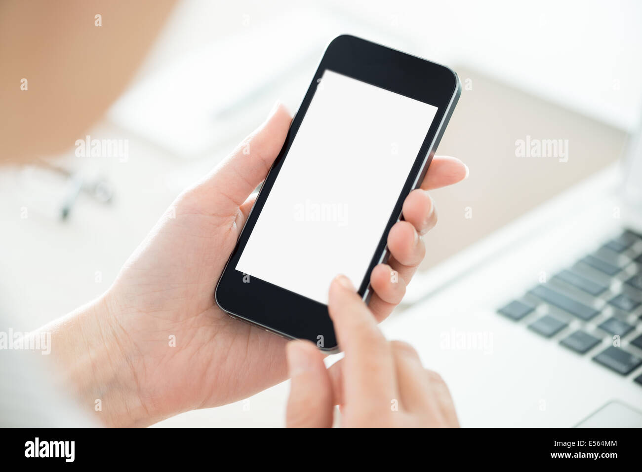 Business person holding modern smartphone and touching on a blank screen. Stylish modern office workplace on a background. Stock Photo