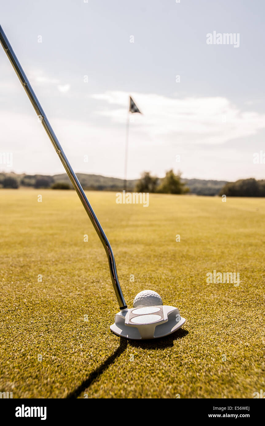 Golfer about to putt a white golf ball on the green towards a black and