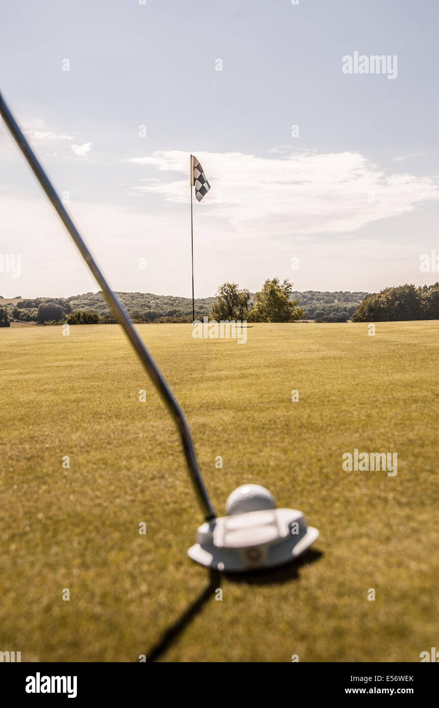 Golfer about to putt a white golf ball on the green towards a black and white checkered flag Stock Photo