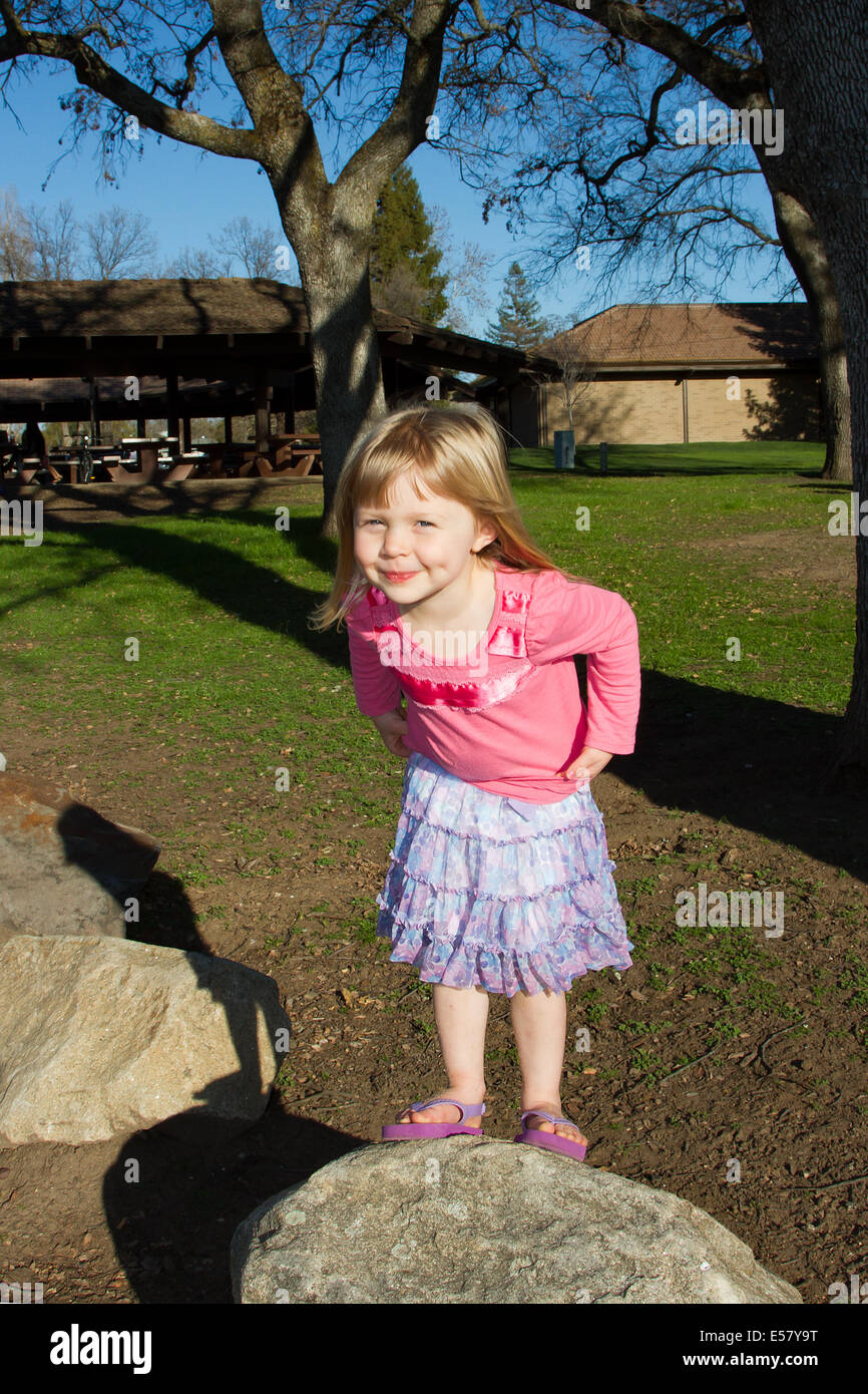 Young Caucasian girl playing in the park. She is wearing a pink t-shirt and blue skirt. Stock Photo