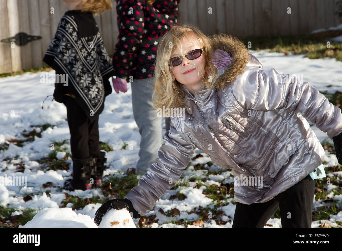 Family snow fun, Young blond girl wearing sunglasses making snowballs. Stock Photo