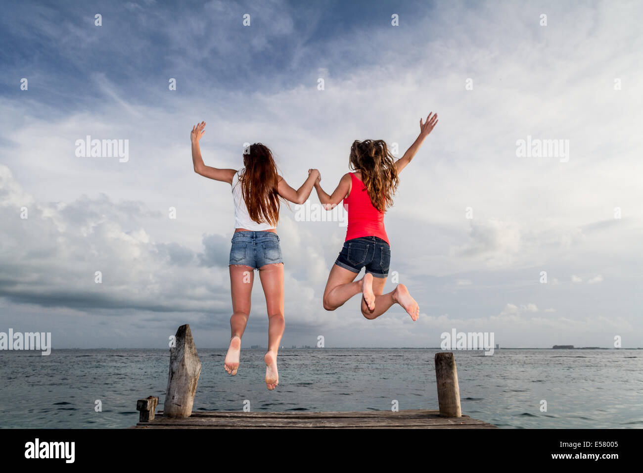 Two young girls jumping in happiness in a stunning seascape at the pier Stock Photo