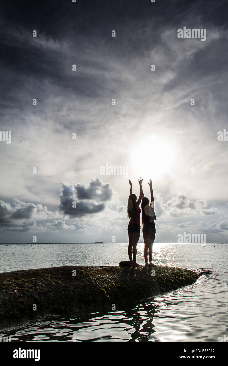 Two young woman praising at the sky at sunset by the sea Stock Photo