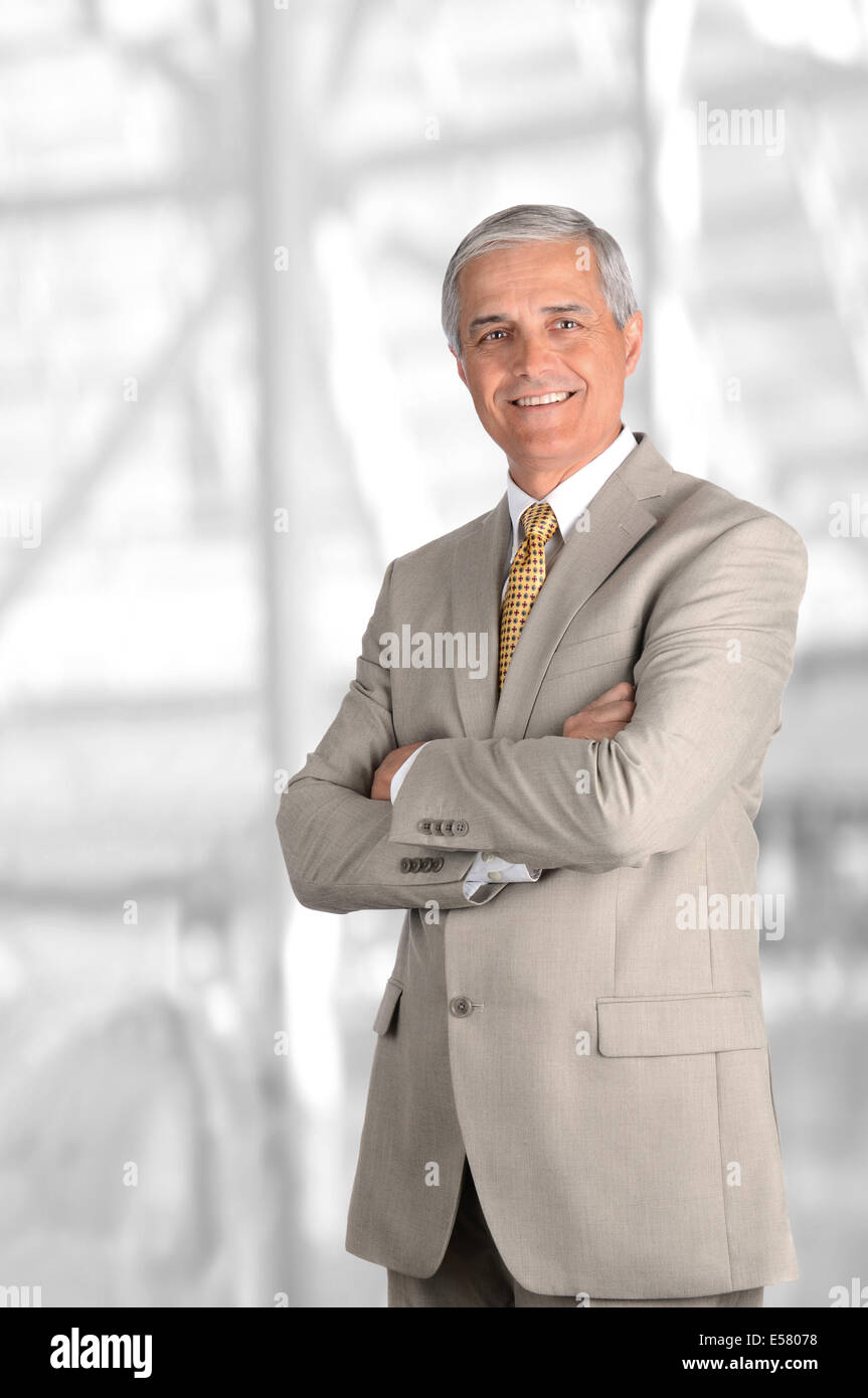 A mature businessman with his arms folded against blurred modern office interior. Vertical Format. Stock Photo