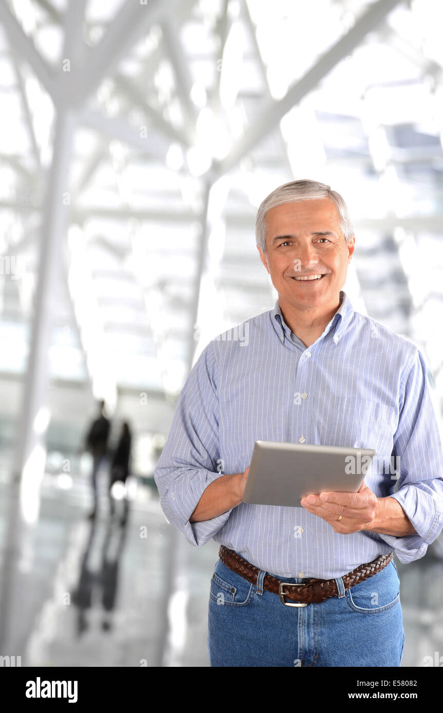 A mature businessman in the lobby of a modern office building. The casually dressed man is smiling and there are blurred people Stock Photo