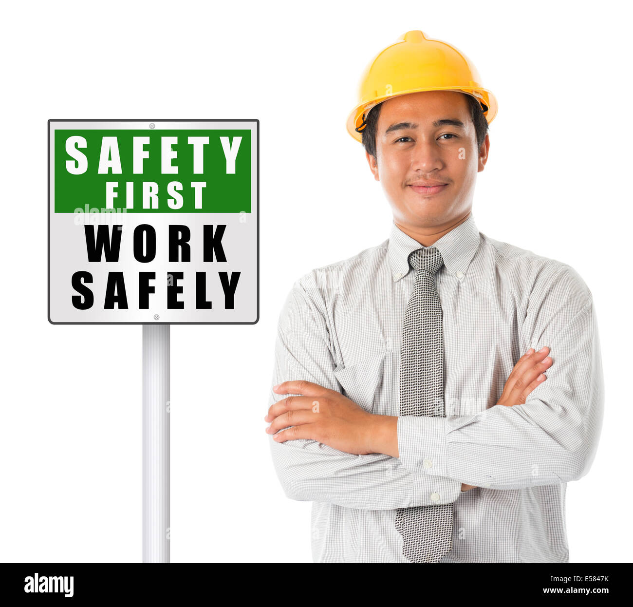 Asian male worker wearing a hardhat smiling and looking at camera, arms crossed standing beside safety first sign board, isolate Stock Photo