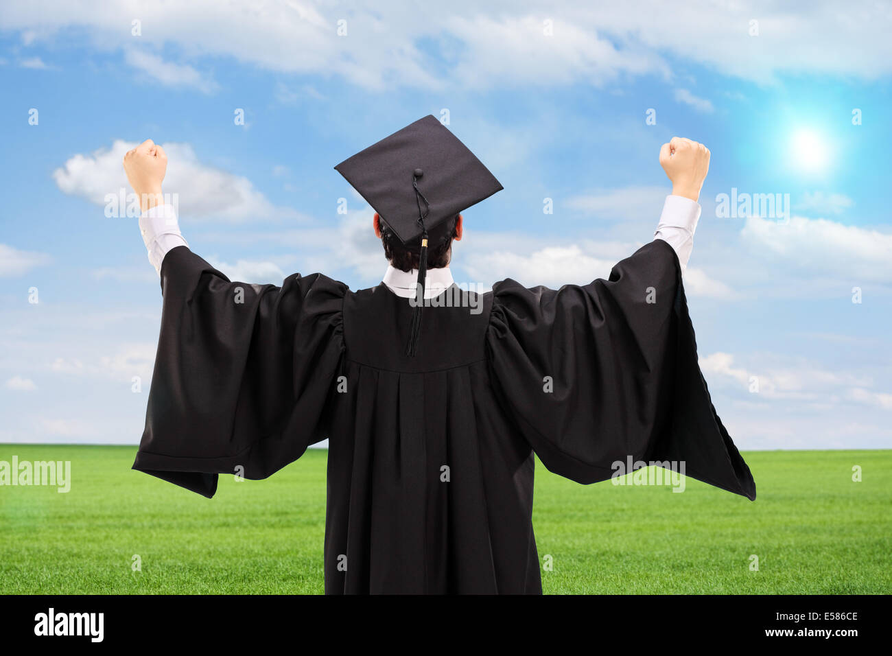 Male graduate gesturing happiness in an open field, rear view Stock Photo
