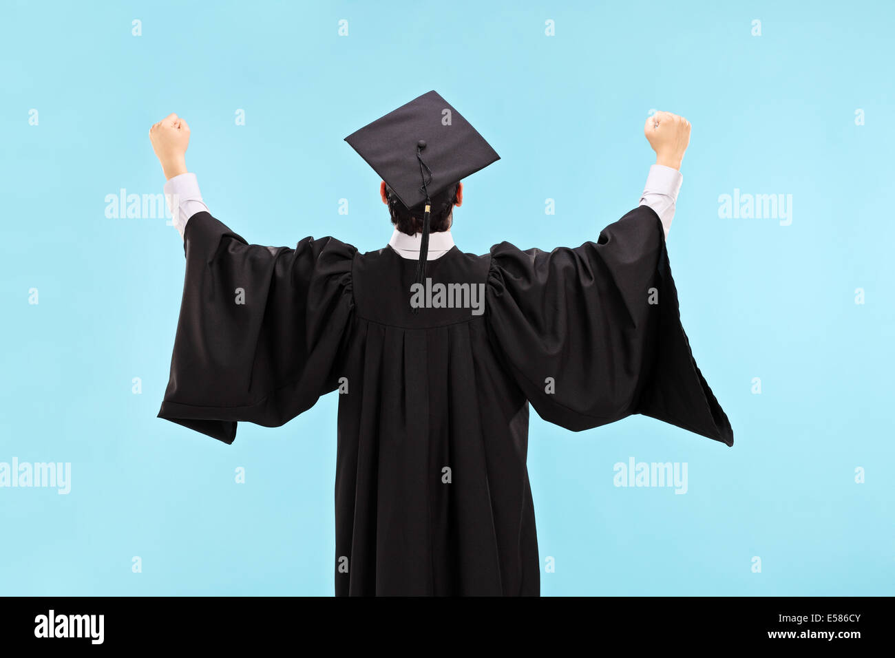 Overjoyed graduate student with raised fists on blue background, rear view Stock Photo