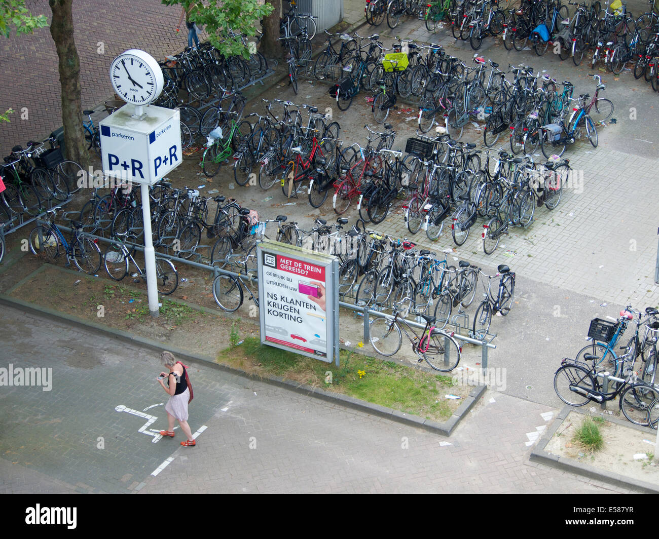Bicycle parking area at Breda train station with woman looking at her smartphone. Breda, the Netherlands. Stock Photo