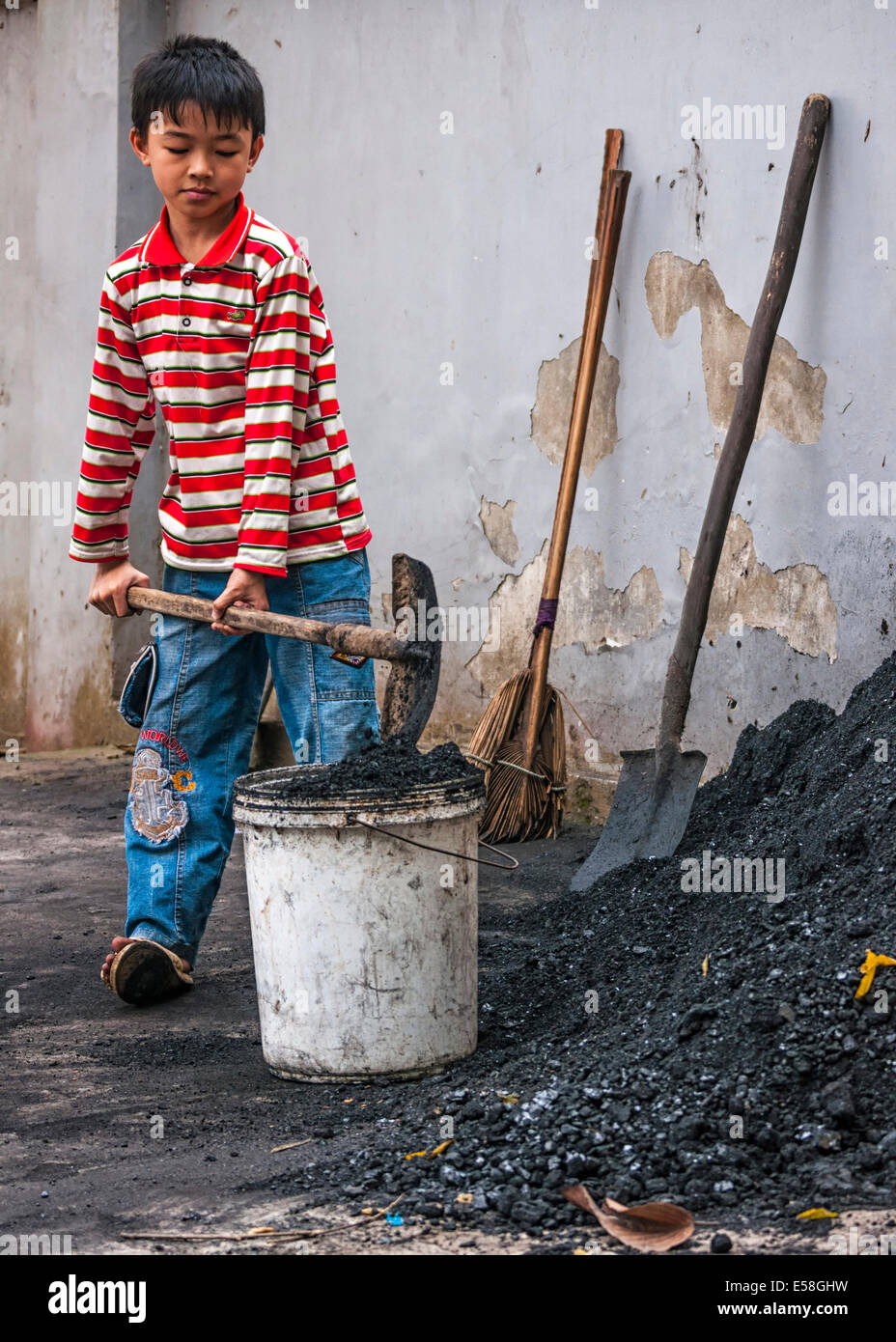 Child labor, boy scoops coal in bucket. Stock Photo