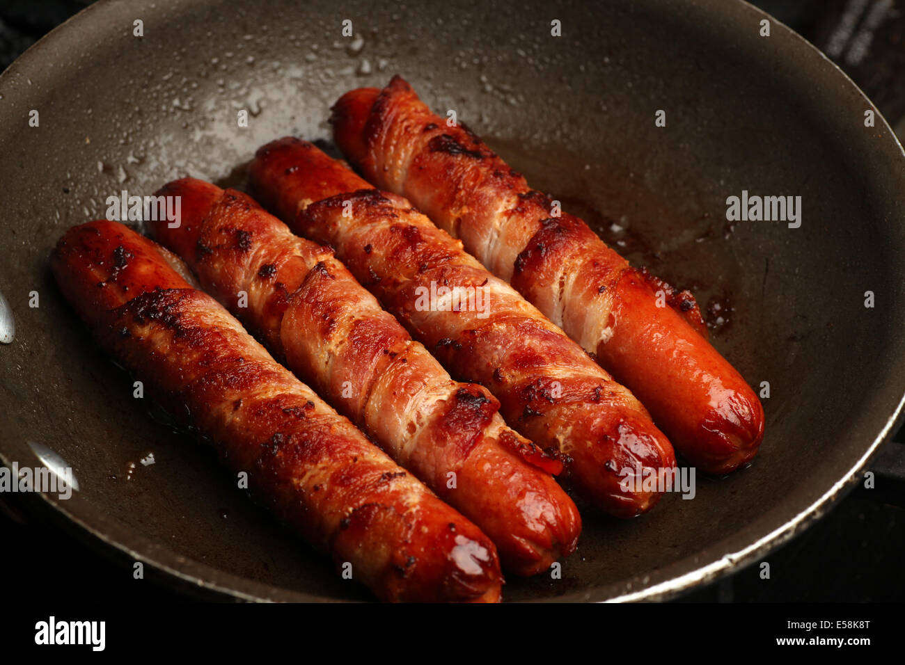 View of hot dogs wrapped in bacon in fry pan Stock Photo