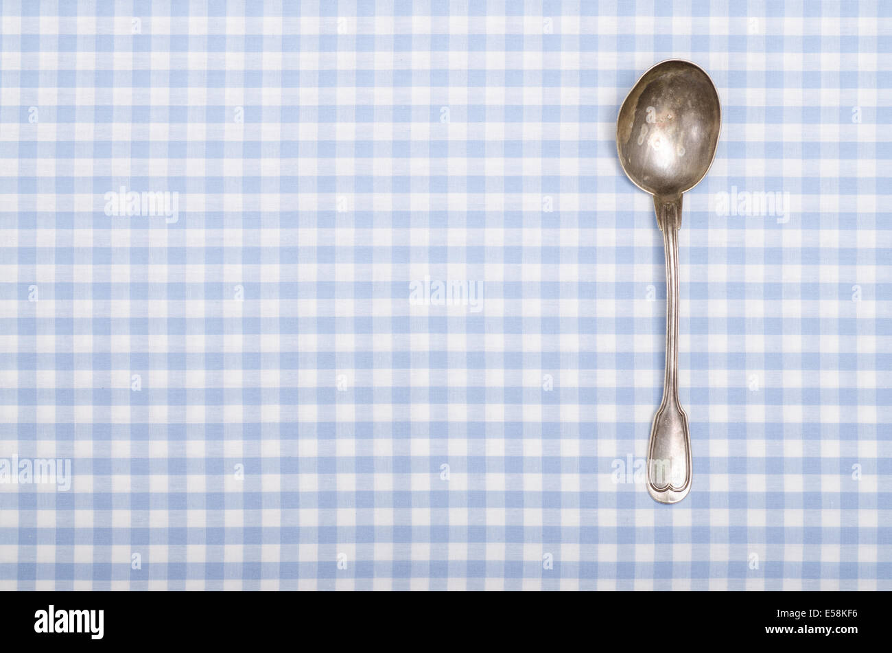 Old silver spoon on blue and white vichy table cloth with text space Stock Photo