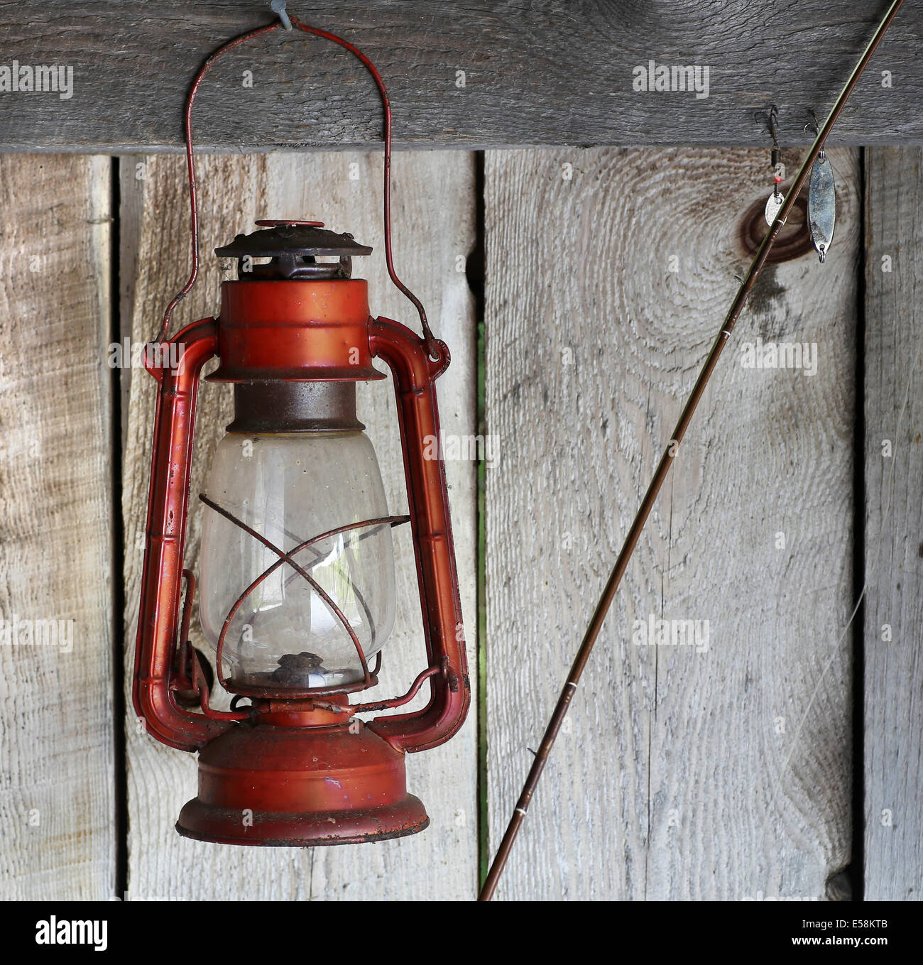 Red lantern hanging on rough wood cabin wall with fishing rod and hook nearby Stock Photo