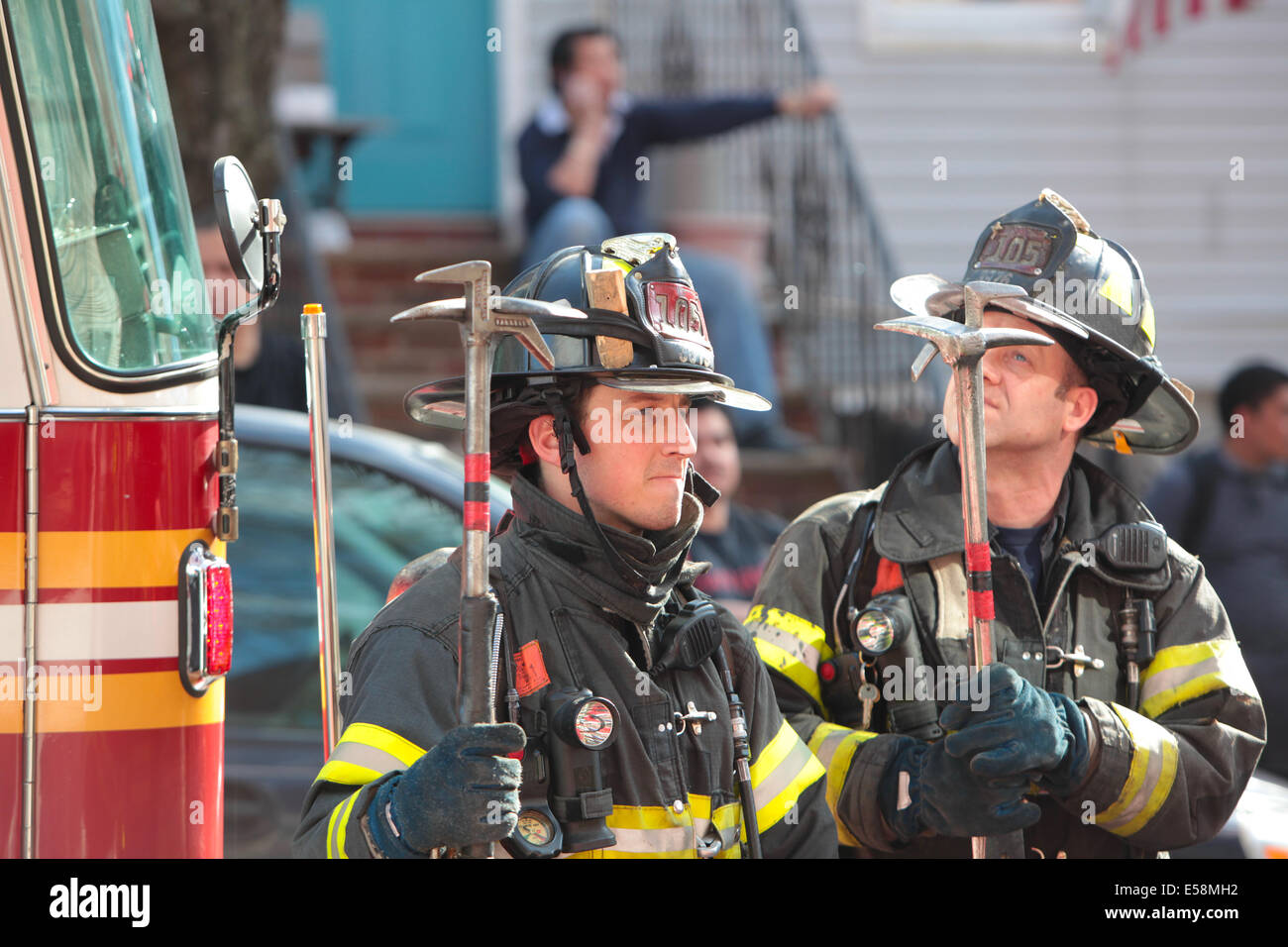 FDNY firefighters stand by with tools in residential neighborhood fighting row house fire Stock Photo