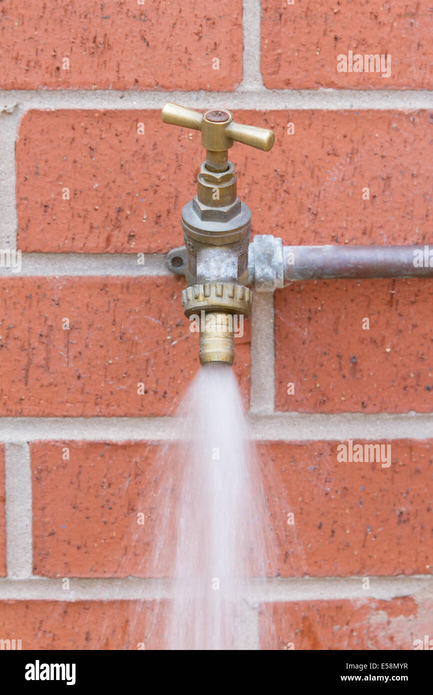 Outside tap on brick wall wasting water Stock Photo