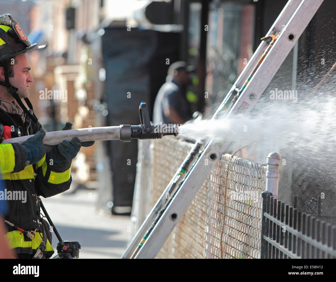 New York City - Firefighter uses hose to spray high pressure water on residential fire in Gowanus, Brooklyn Stock Photo