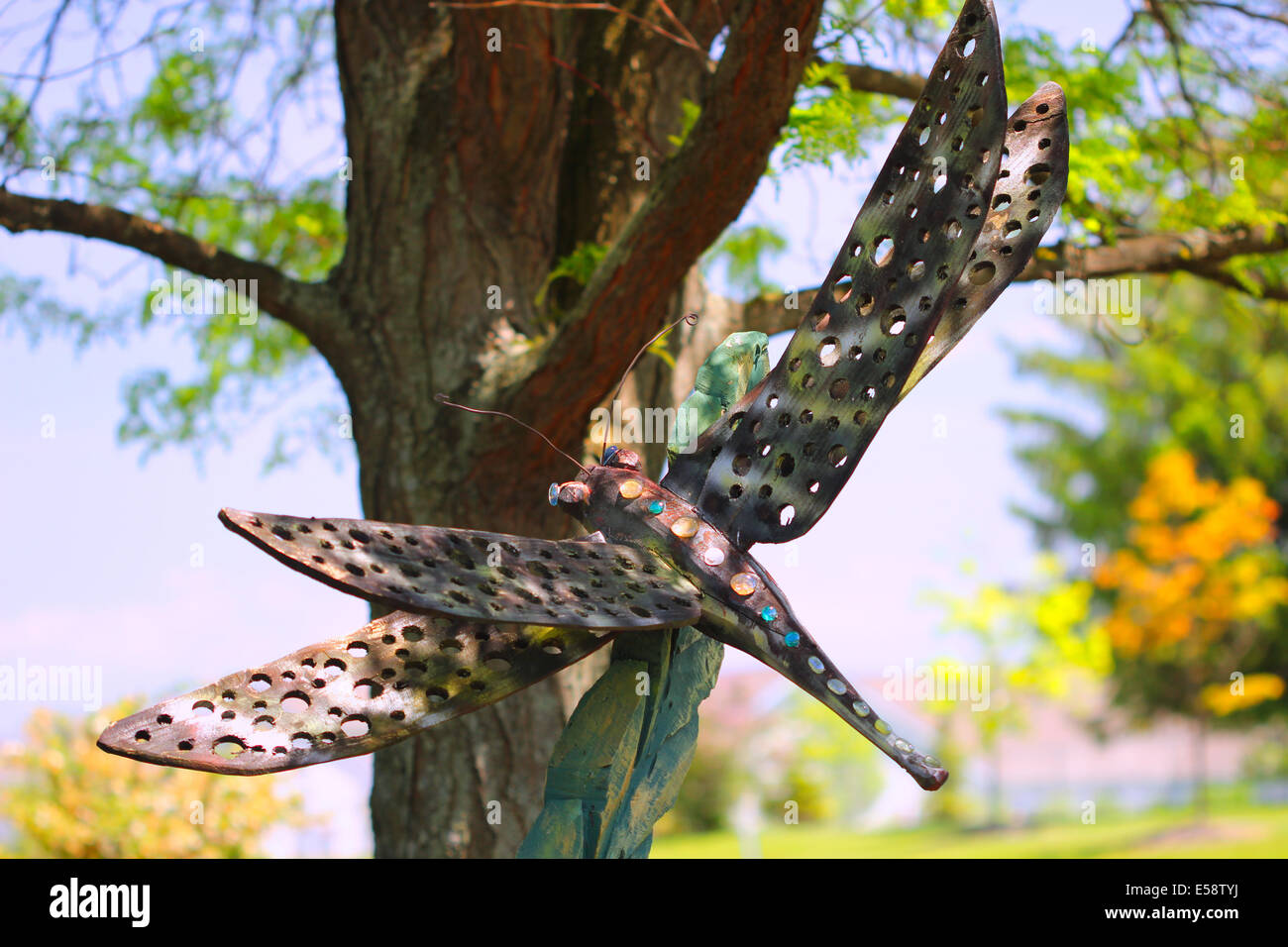 A garden ornament standing by a tree in the shape of a dragonfly insect. Stock Photo